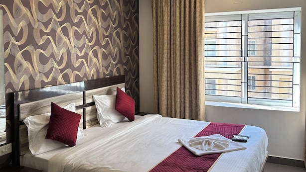 A hotel room with a large bed, a ceiling fan, a window with bars, and a patterned wall. - Jagannath Puri Beach Stay (Brahmagiri)