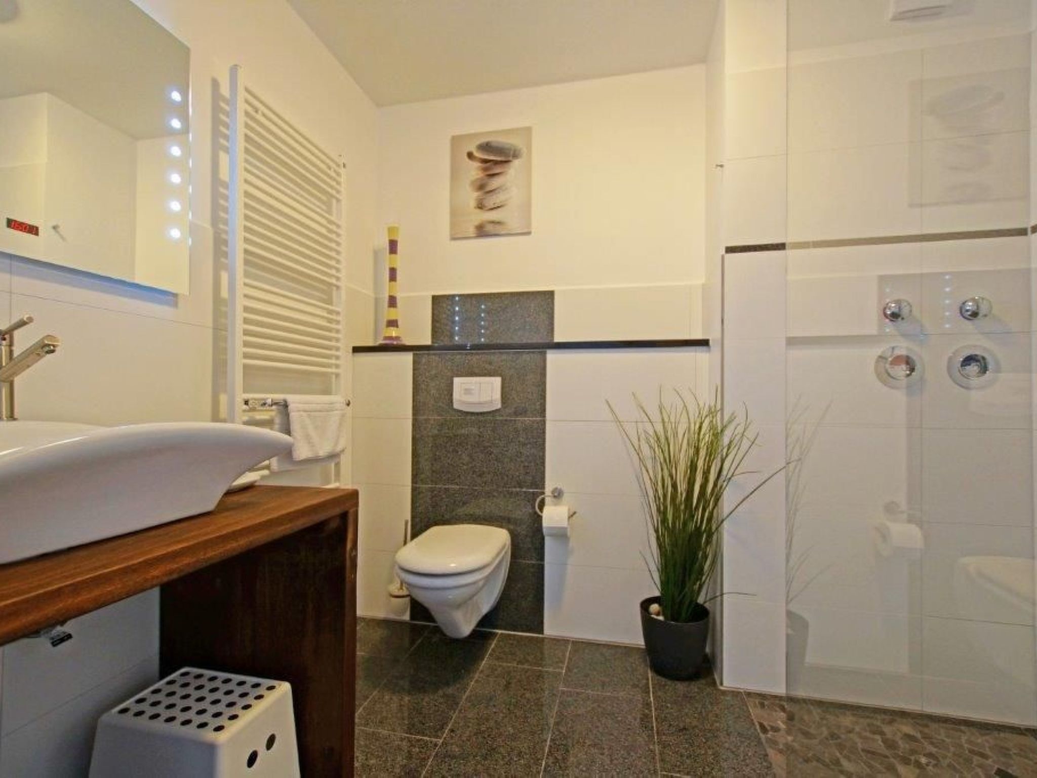 A modern bathroom with a white sink, a toilet, a shower, and a potted plant.