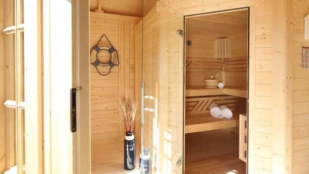 Un sauna en bois avec une porte en verre, un panneau d’accueil et des serviettes rangées sur des étagères.