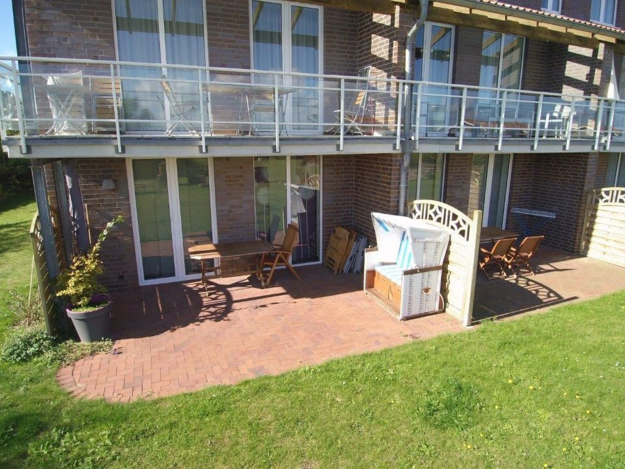 Un bâtiment à deux étages doté d’un patio couvert comprenant une table et des chaises, un canapé en osier et un petit jardin agrémenté d’une plante en pot.