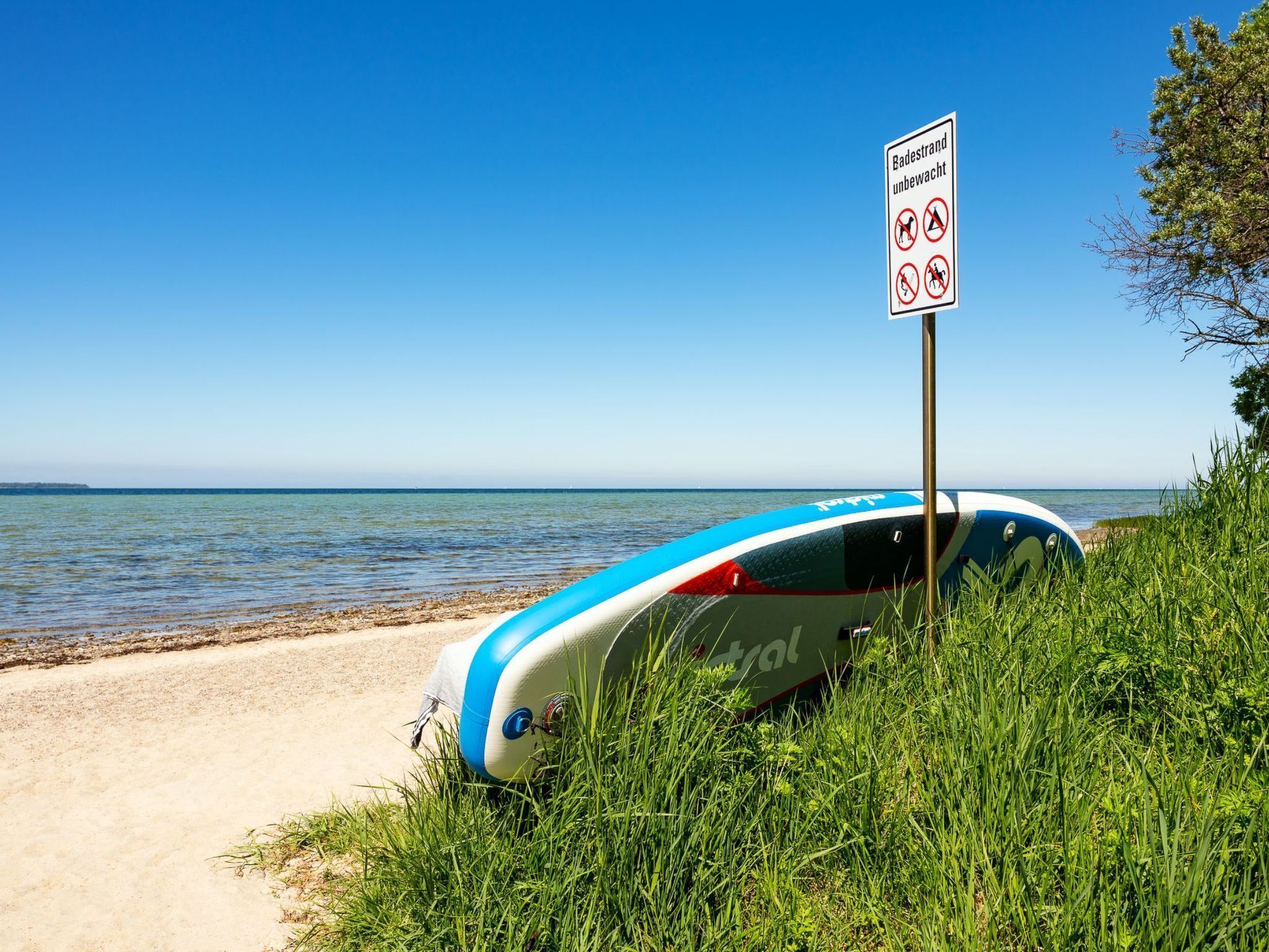 Ein Strand mit einem Schild, das das Schwimmen und Tauchen verbietet. Ein blau-weißes Schlauchboot ist teilweise im Sand vergraben.