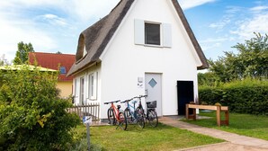 Een wit gebouw met een steil dak, een klein raam en een deur. Fietsen staan er voor geparkeerd.