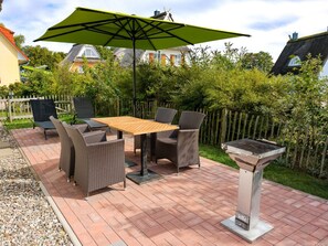 Un patio al aire libre con mesa y sillas, una parrilla y un paraguas verde.