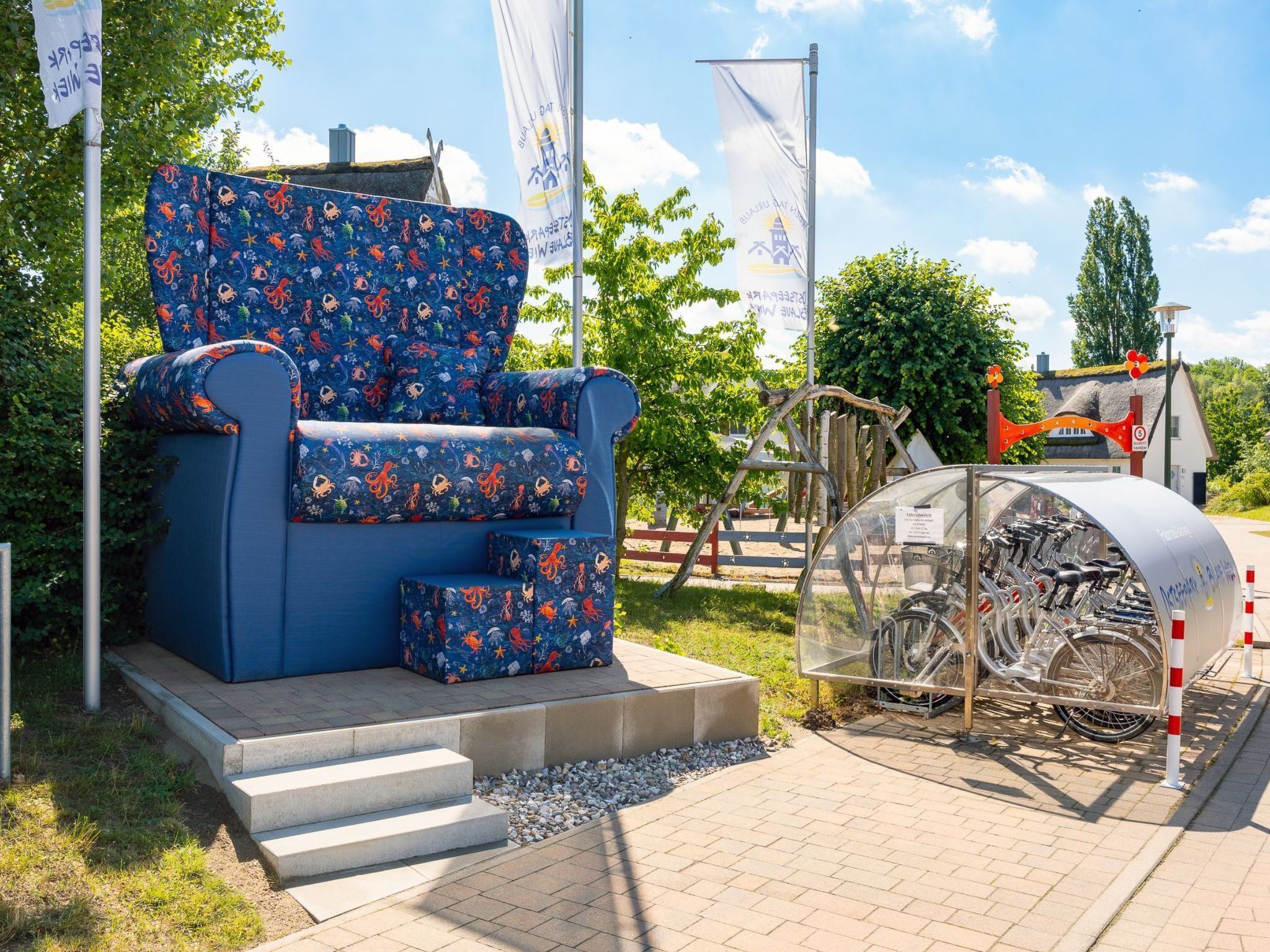 Un sillón azul con un estampado de temática espacial, un mueble transparente para guardar bicicletas y un pequeño edificio con techo de paja.