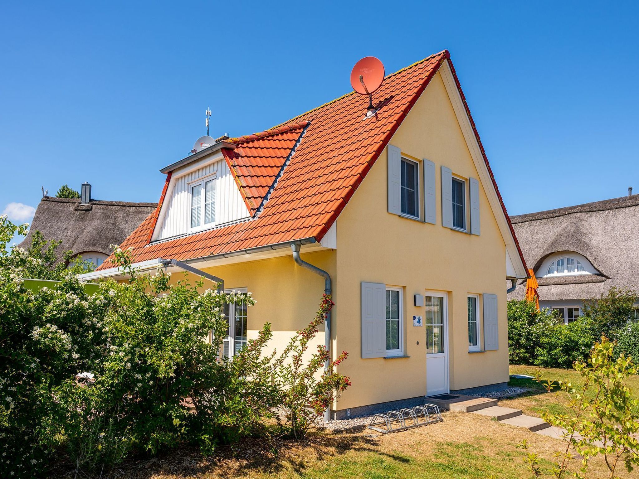 Une maison à deux étages, avec un toit recouvert de tuiles rouges, des volets blancs et une antenne parabolique.