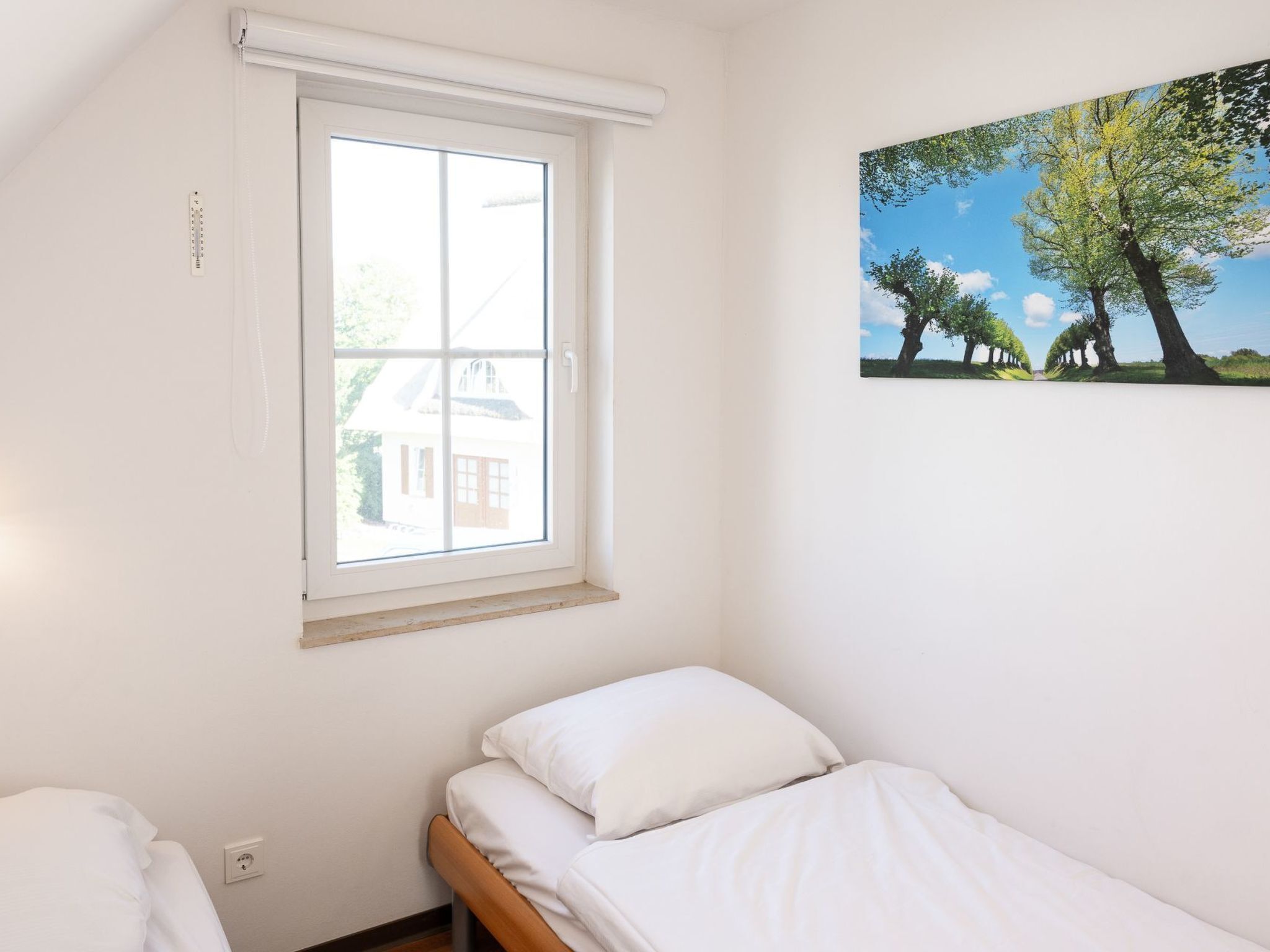 A small, single-bed room with a window and a painting of trees.