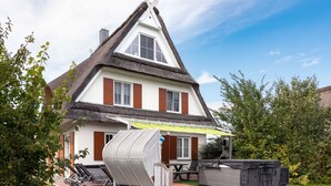 Een huis met rieten dak, witte muren en bruine luiken. Er is een terras met tuinmeubilair en een barbecue.