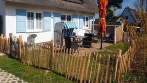 Ein Haus mit einem Reetdach, einem Holzzaun und Gartenmöbeln, darunter ein Tisch und Stühle.