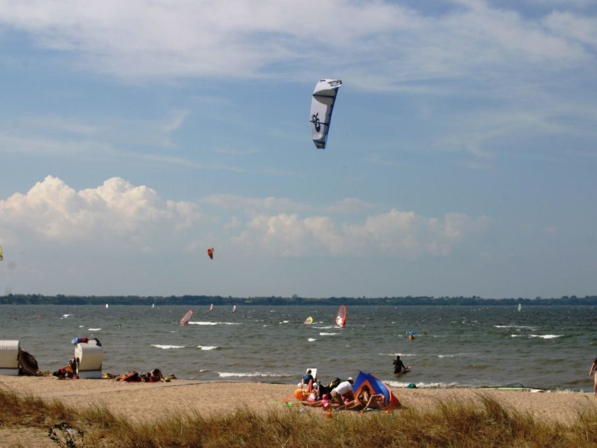 En strand med folk, tält och utrustning för vindsurfing.