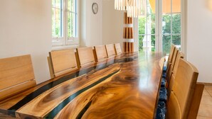 A conference room with a long wooden table and chairs, large windows, and a hanging light fixture.