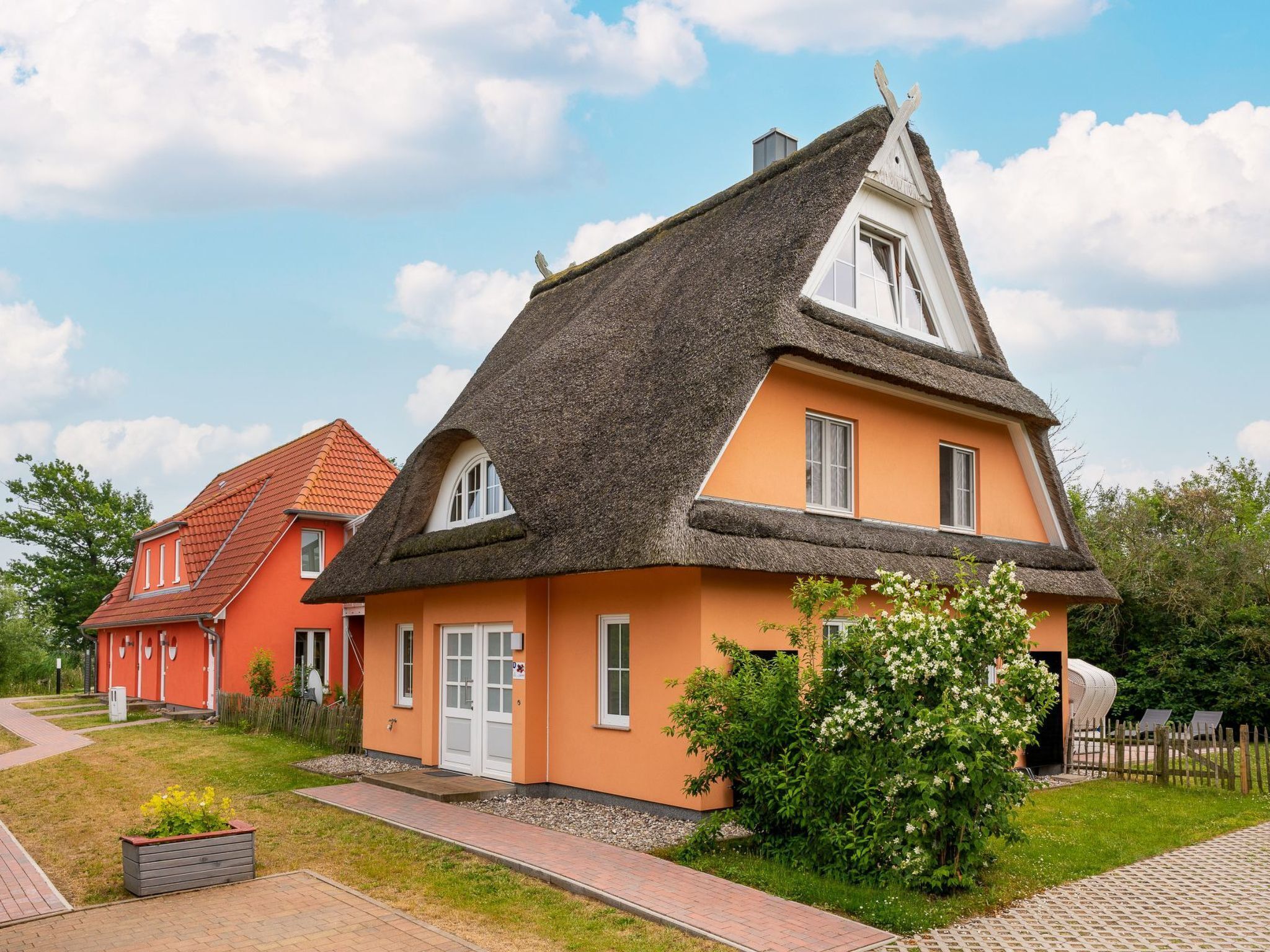 Ein traditionelles Haus mit einem Strohdach, einer kleinen Veranda und einem Garten mit blühenden Pflanzen.