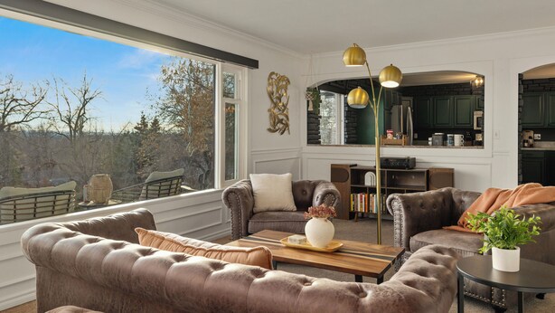 A spacious living room with leather sofas, a wooden coffee table, and a large window offering a view of the outdoors.