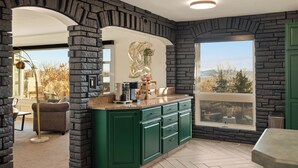 A kitchen with green cabinets, a stone accent wall, and a large window offering a view.