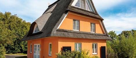 A two-story house with a thatched roof, orange walls, and a small garden.