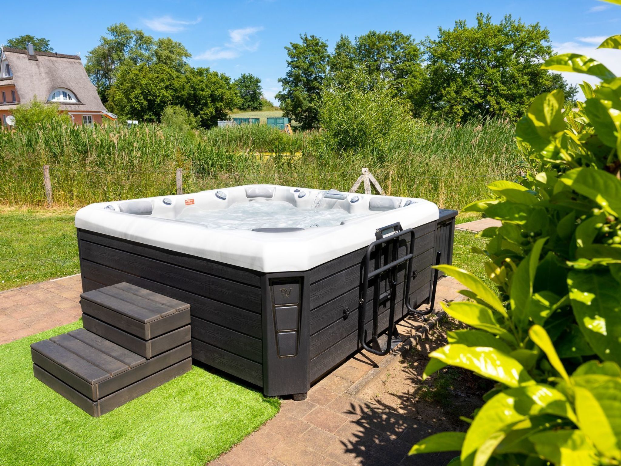 Een hottub met een houten bankje en treden, omringd door een gazon en bomen.