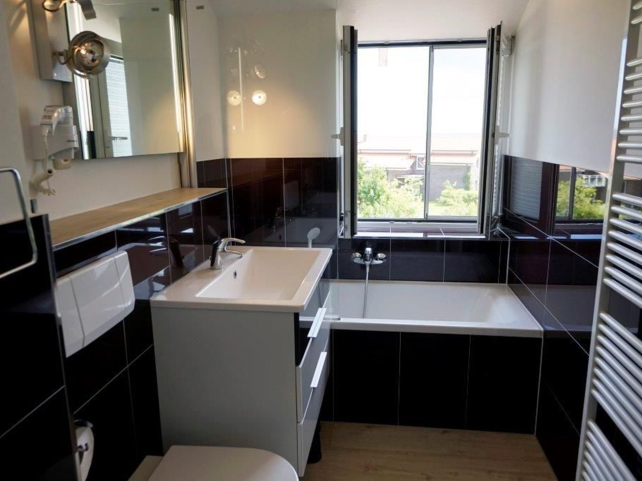 A modern bathroom with a white sink, a mirror, and a window.