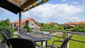 Eine Terrasse mit einem runden Tisch und vier Stühlen, einem überdachten Pergola und Blick auf Häuser im Hintergrund.