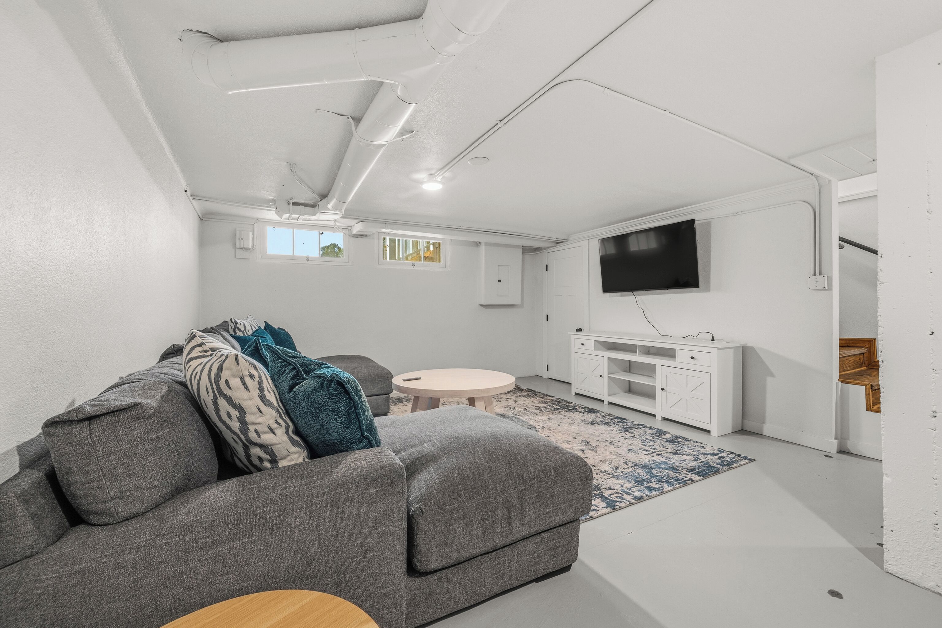 A modern living room with a grey sofa, a round coffee table, and a flat-screen TV mounted on the wall.