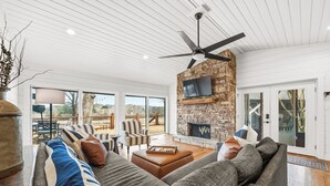 A spacious living room with a stone fireplace, a ceiling fan, and a large window overlooking a deck. - Lake Hamilton Retreat, Main House, Guest House, Sleeps Up to 14, Private Dock (Hot Springs)