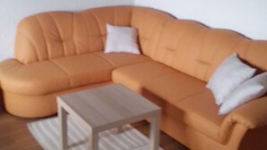 Ein modernes Wohnzimmer mit einem beigefarbenen Ecksofa, einem kleinen Holztisch und einem gemusterten Teppich.