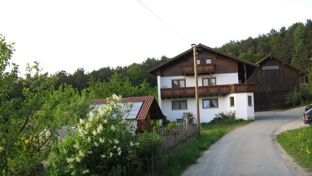 Ein zweistöckiges Haus mit Balkon, Holzzaun und gepflasterter Auffahrt.