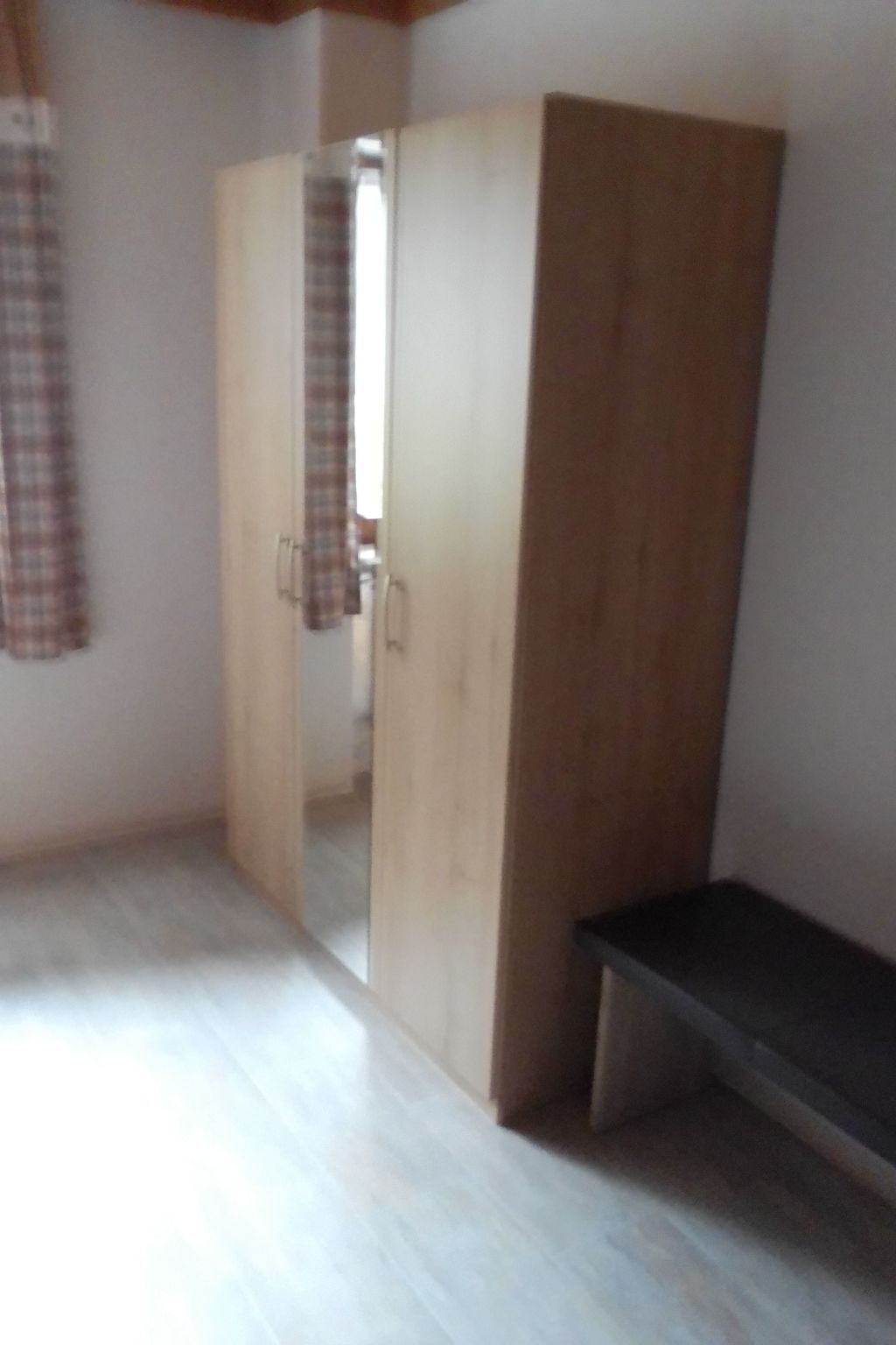 Une pièce comprenant une armoire, un banc et une porte donnant sur une autre pièce.
