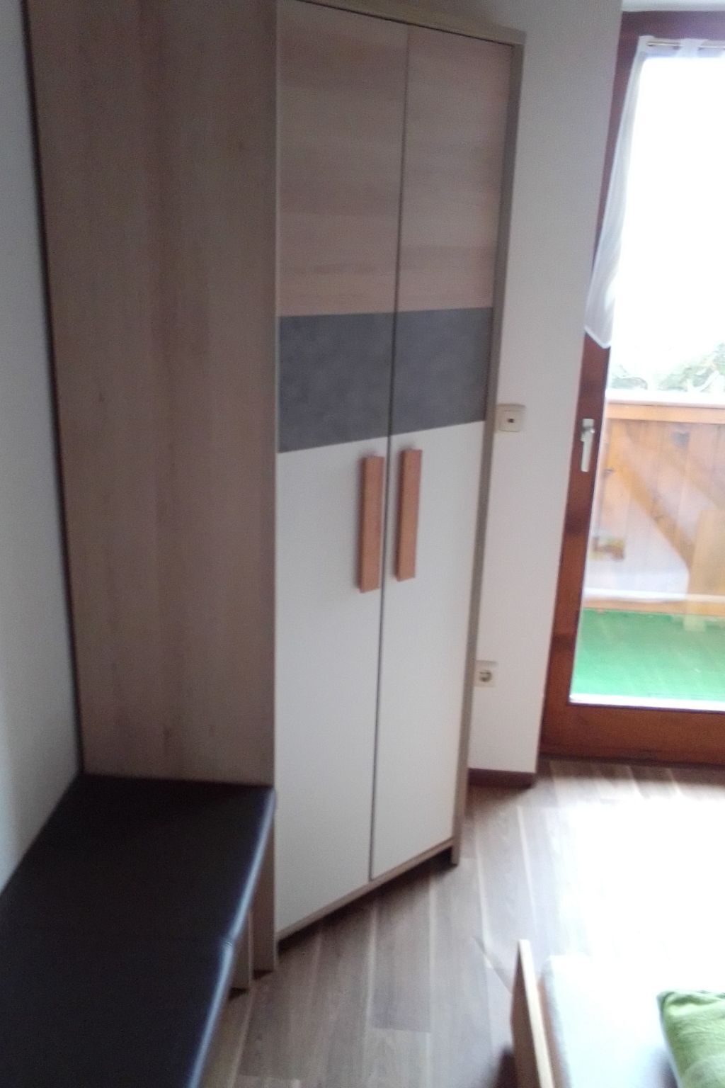 Ein Zimmer mit Schrank, Bank und einer Tür zu einem Außenbereich.