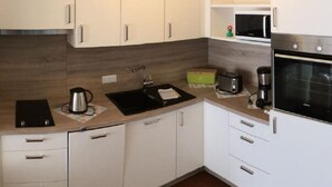 A modern kitchen with white cabinets, a black countertop, a sink, a microwave, and an oven. - Haus Arberblick by Interhome (Zandt)