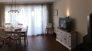 A living room with a dining area, a television on a cabinet, and a window with curtains. - Haus Arberblick by Interhome (Zandt)