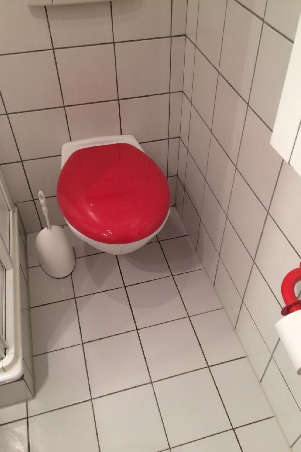 Une petite salle de bain avec des toilettes blanches, un abattant rouge et un bidet blanc.