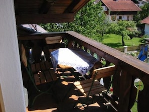 Eine Holzterrasse mit Tisch und Stühlen, umgeben von Grün und Häusern im Hintergrund.