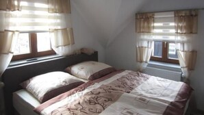 Camera da letto con due letti, soffitto spiovente e finestre con tende.