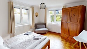 Ein Schlafzimmer mit Bett, Stuhl, Kleiderschrank und zwei Fenstern.