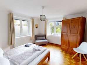 Ein Schlafzimmer mit Bett, Stuhl, Kleiderschrank und zwei Fenstern.