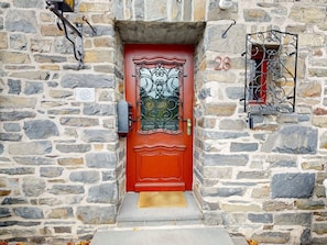 A red door with a decorative glass panel and a metal gate, set in a stone building with a stone wall and a number plaque. - Eifel Oase by Interhome (Monschau)