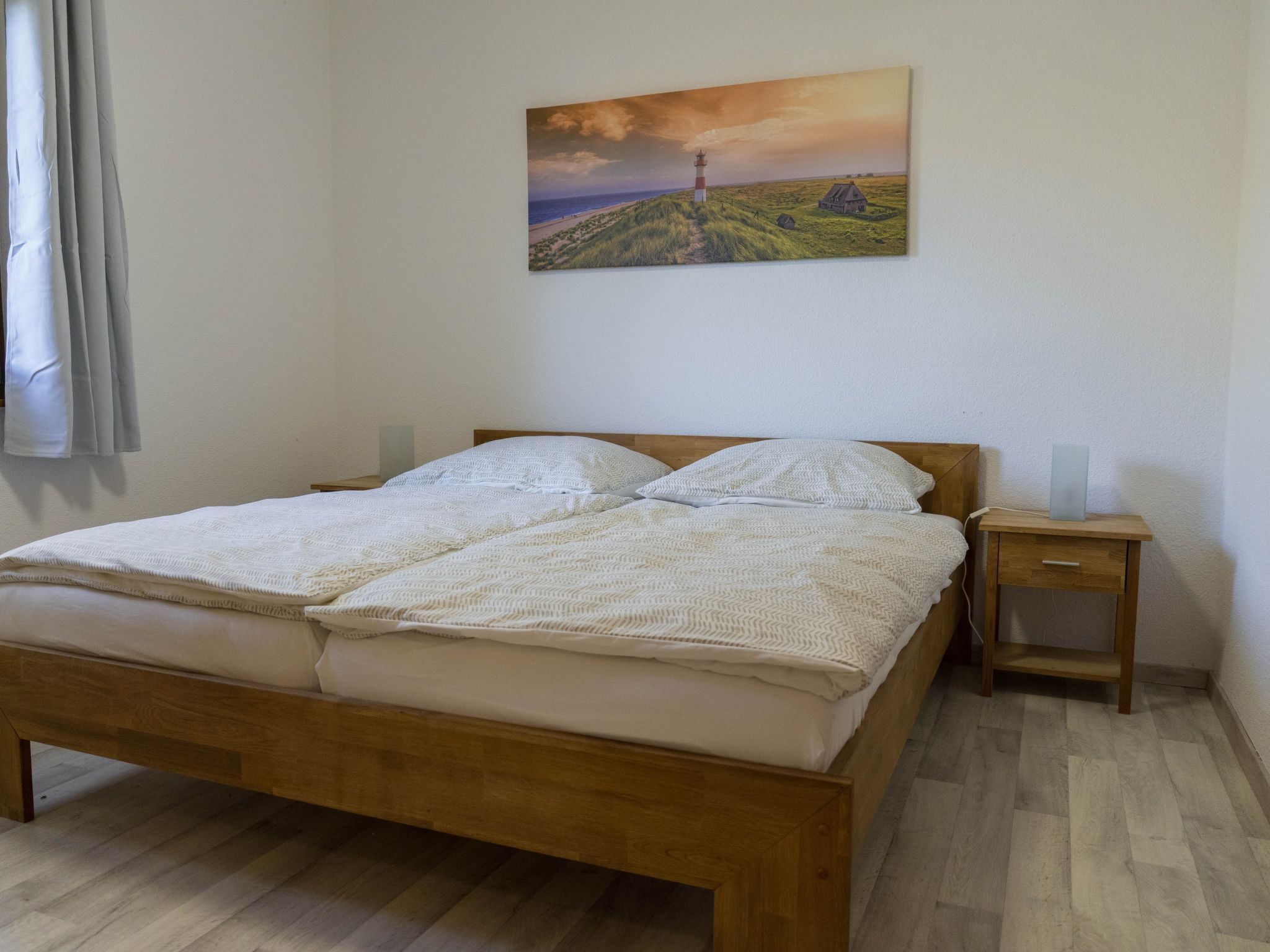 Ein Schlafzimmer mit einem hölzernen Bett, einem Nachttisch und einem Gemälde eines Leuchtturms an der Wand.