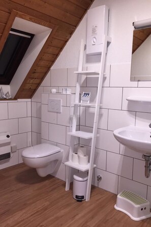 Ein Badezimmer mit Toilette, Waschbecken, einer weißen Sprossenregal und einem weißen Mülleimer.