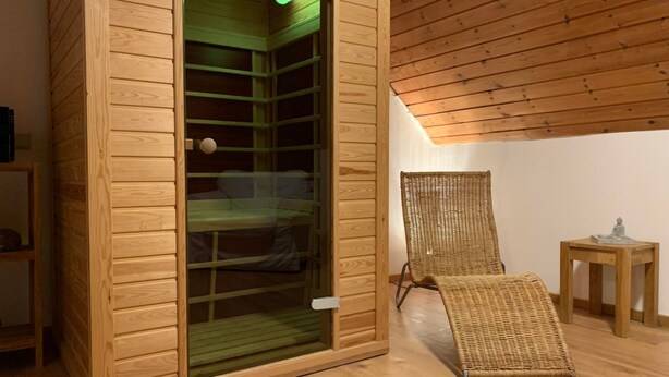 Een sauna met houten wanden en een glazen deur, een rieten stoel en een klein houten tafeltje.