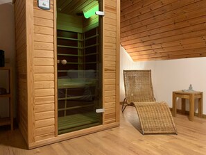 Un sauna aux murs en bois et à la porte en verre, avec un fauteuil en osier et une petite table en bois.