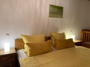 Ein ordentlich bezogenes Bett mit gelber Bettwäsche, einem Holz-Kopfteil und Nachttischlampen.