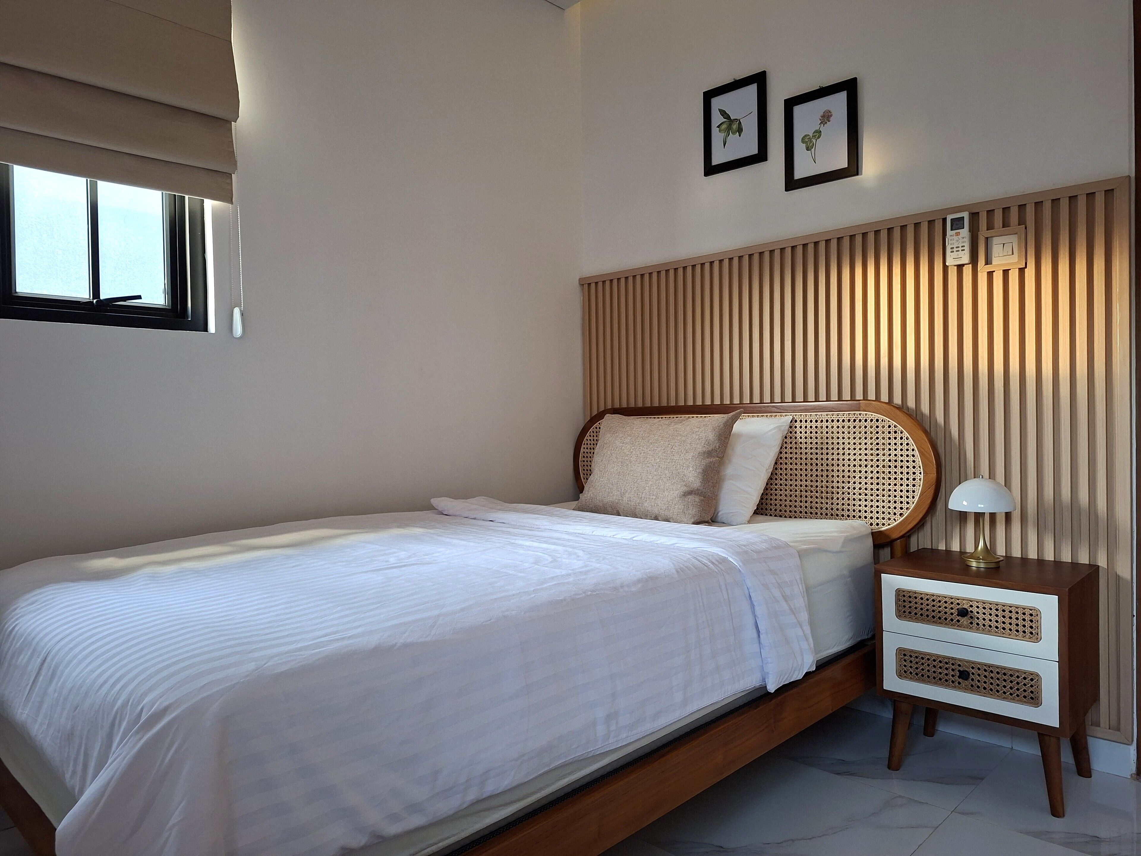 A neatly made bed with a wooden headboard, a bedside table with a lamp, and two framed pictures on the wall.