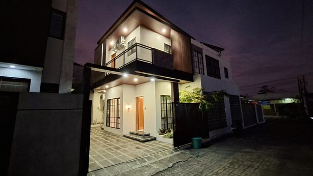 Een modern huis met twee verdiepingen, een balkon, een zichtbare garage en een verharde oprit.