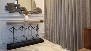 Een hal met een marmeren vloer, een console tafel met een witte vaas en een decoratieve spiegel, en grijze gordijnen.