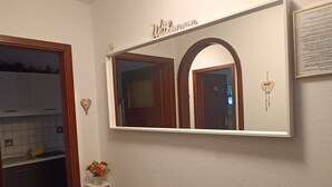 Un baño con un espejo grande, un pequeño estante con adornos y un cartel sobre el espejo.