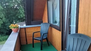 Un balcón con dos sillas, una mesa, paredes de madera y una alfombra verde.