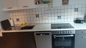 Una cocina con armarios blancos, lavavajillas, horno y pileta.