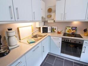 A modern kitchen with white cabinets, a stainless steel sink, a coffee maker, a microwave, and a stove. - Haus Christiane by Interhome (Hage)