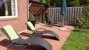 Pieni patio, jossa on kaksi aurinkotuolia, puinen aita ja pieni puutarha-alue.