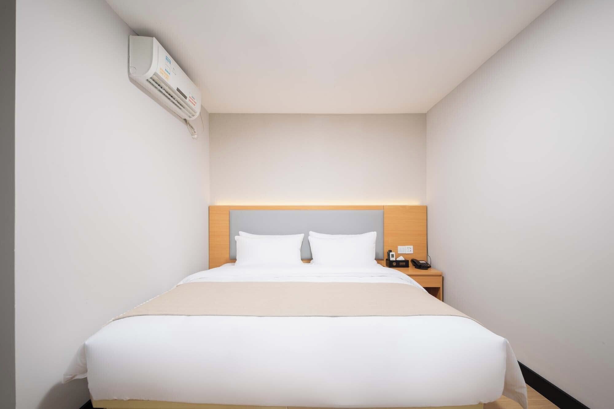Ein Hotelzimmer mit einem Bett, einem Nachttisch mit Telefon und einer an der Wand befestigten Klimaanlage.