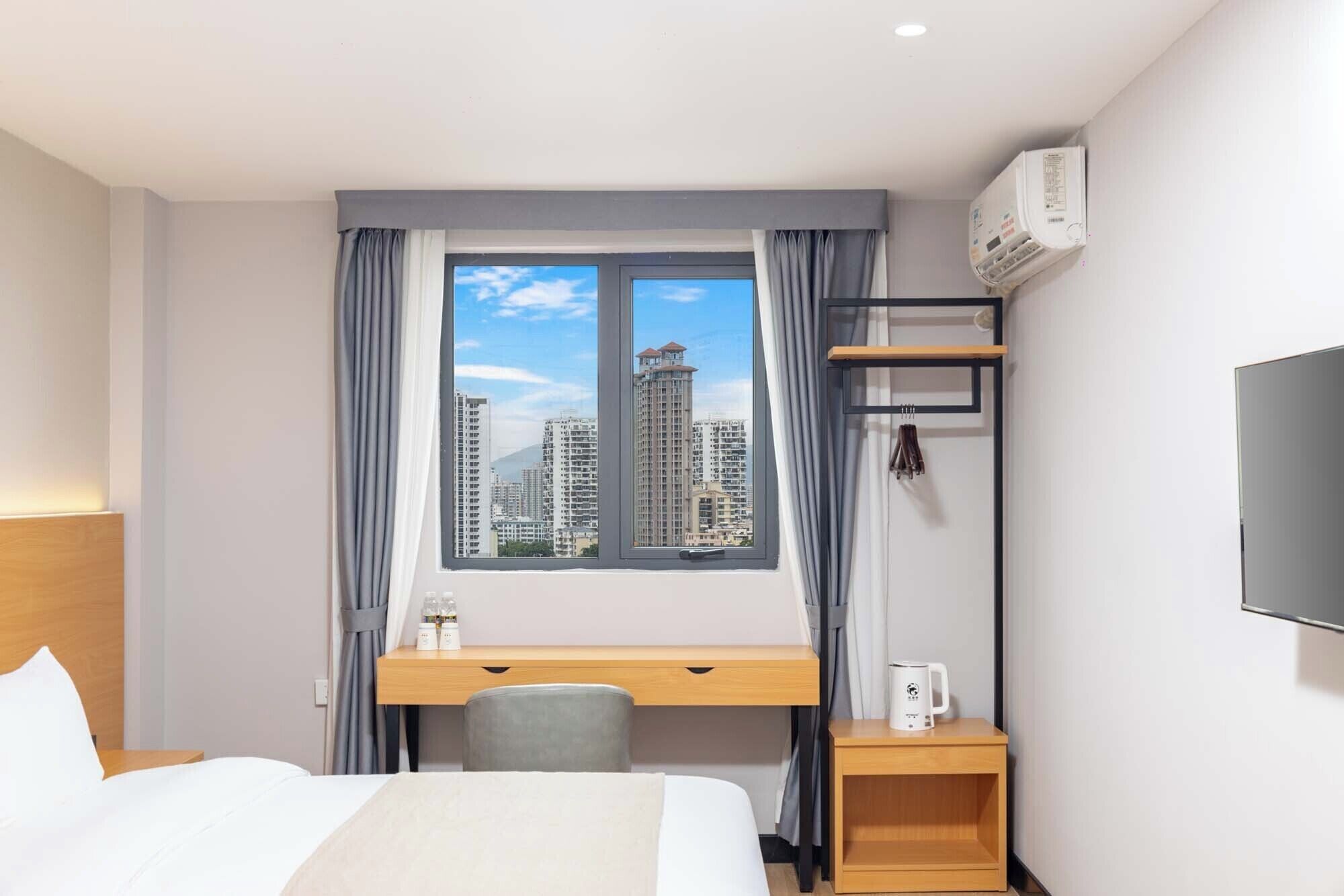 Habitació d'hotel amb llit, escriptori, cadira, televisió i finestra amb vista a la ciutat.